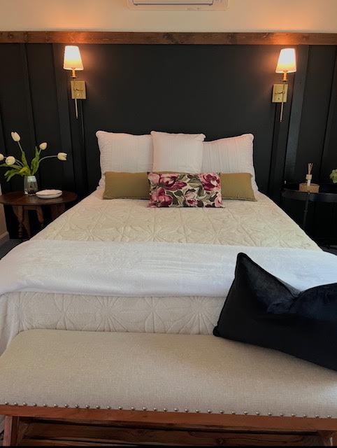 Finished bedroom with black board and batten paneling, brass wall sconces, layered white bedding, and an upholstered bench